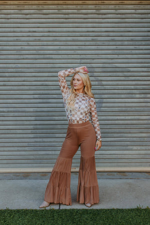 Woman in a patterned top and brown flared pants standing against a metallic shutter.