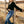Woman in black top and blue jeans leaning against a wooden fence in a field.