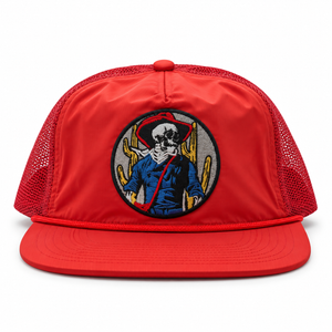 A red snapback hat with a flat brim, red mesh back panels, and a circular embroidered patch on the front featuring a skeleton cowboy with a cactus hat and yellow cacti.