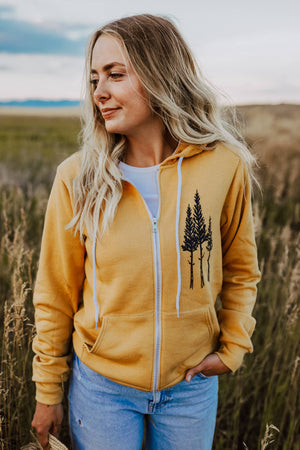 Woman wearing a yellow hoodie with tree design in a natural setting