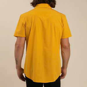 Person wearing a mustard yellow short-sleeve shirt on a beige background