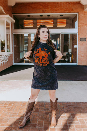 Woman wearing a graphic t-shirt and boots standing in front of a building entrance.