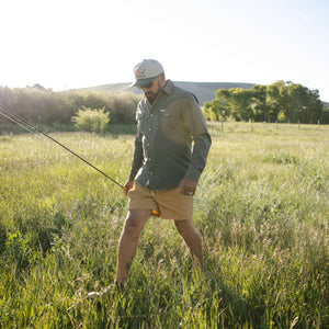 Man holding a fishing pole in a grassy field with trees in the background