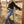 Woman in black top and blue jeans leaning against a wooden fence in a field.