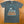 Gray t-shirt with 'Johnny Paycheck' graphic on a brown surface