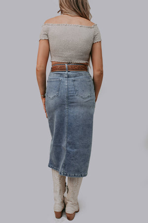 Person wearing a light gray off-shoulder top and blue denim skirt on a plain background