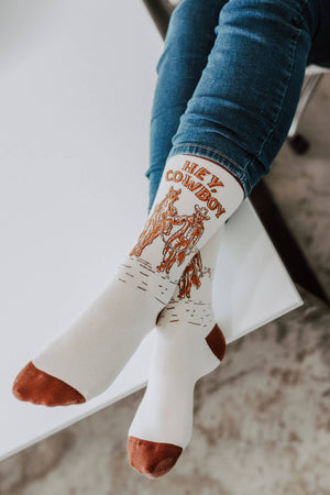 White sock with cowboy design and text, worn by a person sitting on a white surface.
