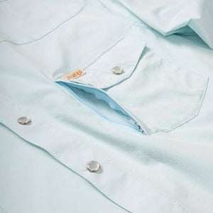 Close-up of a light blue shirt with buttons and a brand logo.