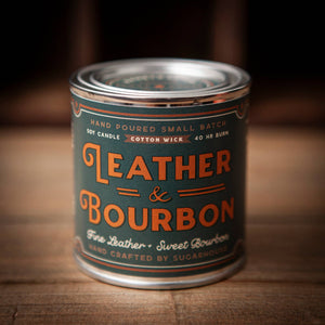 Candle in a can labeled 'Leather & Bourbon' on a wooden surface