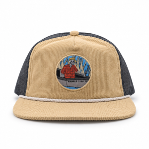 A corduroy snapback hat in tan and dark gray mesh, featuring a circular embroidered patch on the front with a cartoon fisherman and the text 'RAMBLE 2796 FE'.