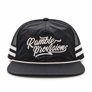 A black trucker-style cap with a flat brim, black mesh back, and white embroidered text reading 'Ramble Provisions' on the front, plus white stripe accents on the sides.