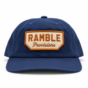 A navy blue baseball cap with a front patch reading 'RAMBLE Provisions' in orange and cream embroidery, shown on a clean white background.
