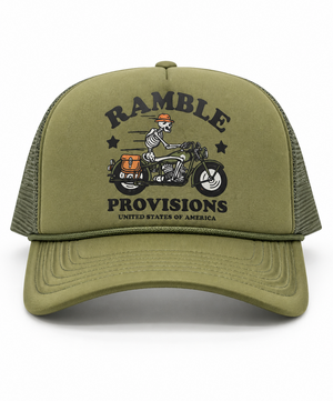 An olive green trucker hat with a graphic on the front panel showing a cowboy riding a motorcycle and the text 'RAMBLE PROVISIONS'. The hat features a structured front panel and dark olive green mesh back panels, photographed against a clean white background.