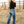 Woman wearing blue jeans and a black top standing in a field with a wooden fence in the background.