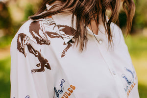 Person wearing a white shirt with horse designs and text, outdoors.