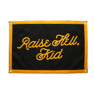 A rectangular black flag with the phrase 'Raise Hell, Kid' screen-printed in gold lettering, with gold details along the edges.