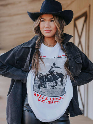 Woman wearing a white t-shirt with a graphic design and text, black jacket, and cowboy hat.