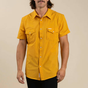 Man wearing a mustard yellow short-sleeve shirt against a beige background