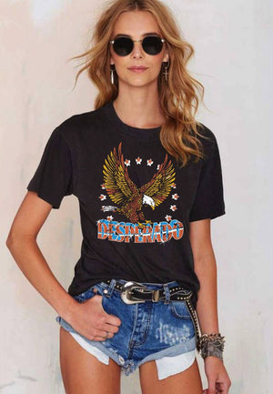 Woman wearing a black t-shirt with an eagle graphic and 'Desperado' text, paired with denim shorts.