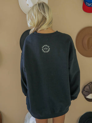 Person wearing a black sweatshirt with a logo on the back against a beige wall.