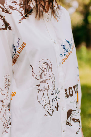 White shirt with cowboy-themed graphics and text on a blurred outdoor background