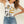 Woman wearing a white tank top with graphic design and text, paired with blue jeans on a plain background